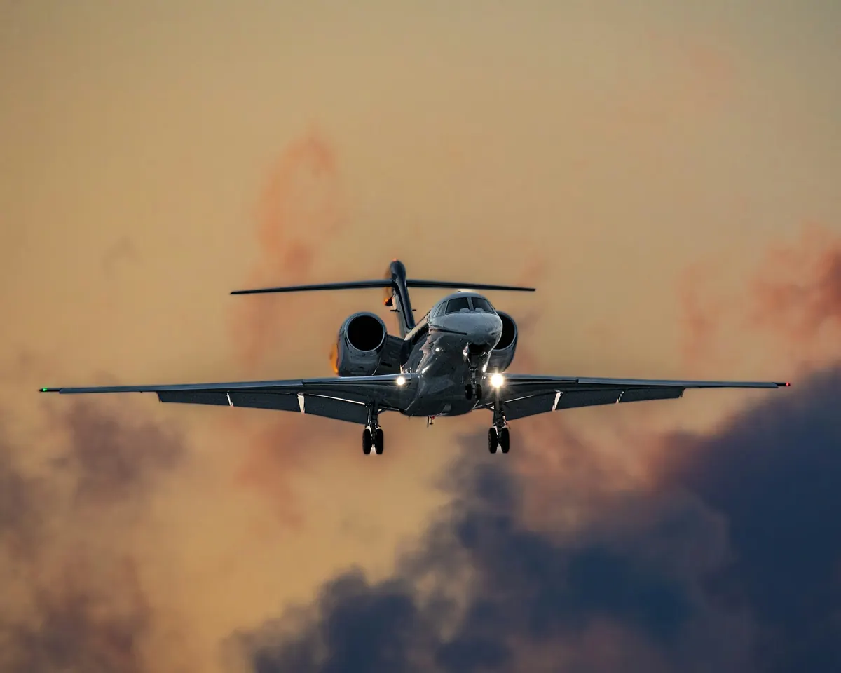Private jet descending toward the runway through amber evening cloud